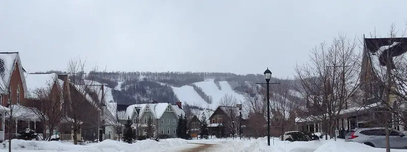 A residential street after a snowfall, with houses and hills behind