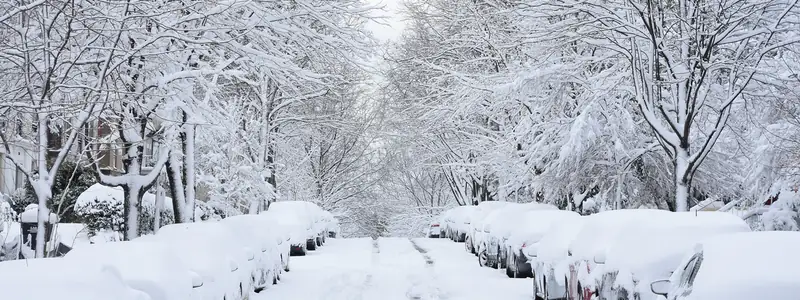 Snow-covered residential street lined with parked cars